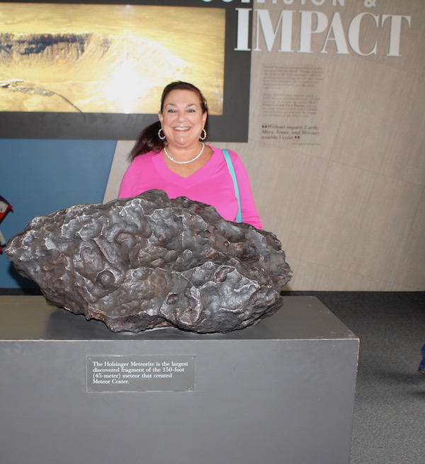 A woman in a hot pink sweater behind a display of a large meteor.