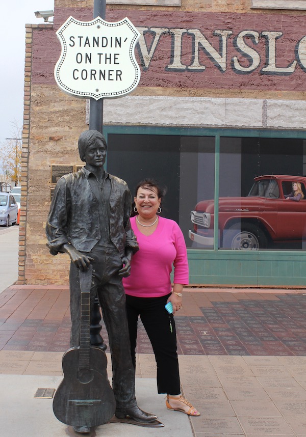 A street corner with a sculpture of a man and a woman in a hot pink sweater standing next to it.