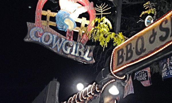 The outside of a western restaurant with a sign the says Cowgirl BBQ and Saloon.