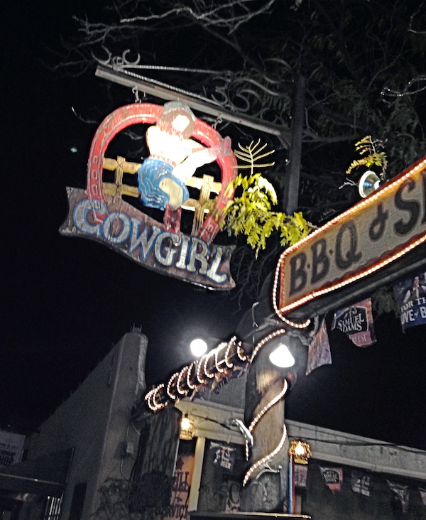 The outside of a western restaurant with a sign the says Cowgirl BBQ and Saloon.