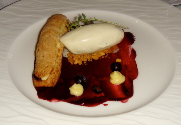 A white plate topped with a long profiterole, a vanilla ice cream quenelle, blackberry sauce and fresh fruit.
