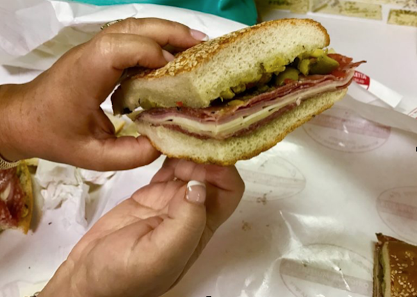 A pair of a woman's hands holding a large Italian sandwich over white deli paper.