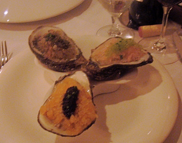 A white plate with three oyster shells filled with three different oyster preparations