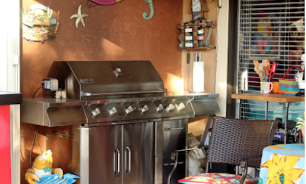 A huge stainless steel gas grill in front of a brown wall