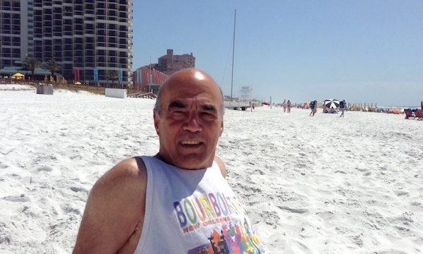 A bald man in a tank top sitting on the sand