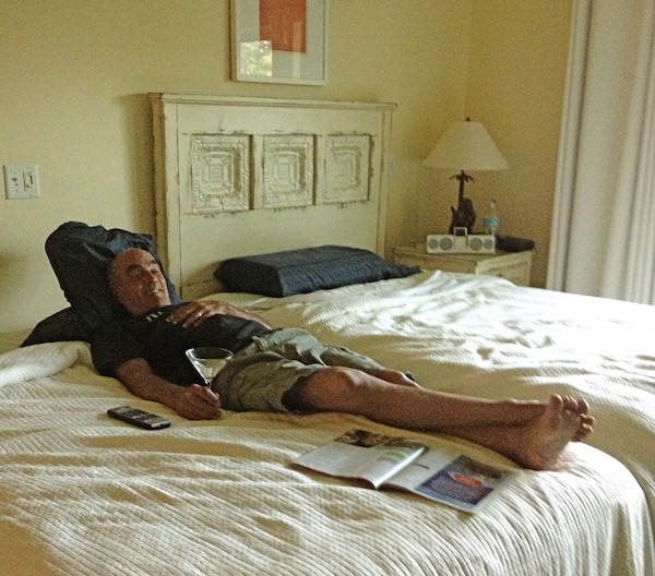 A man in shorts lying on a bed with a martini in his hand.