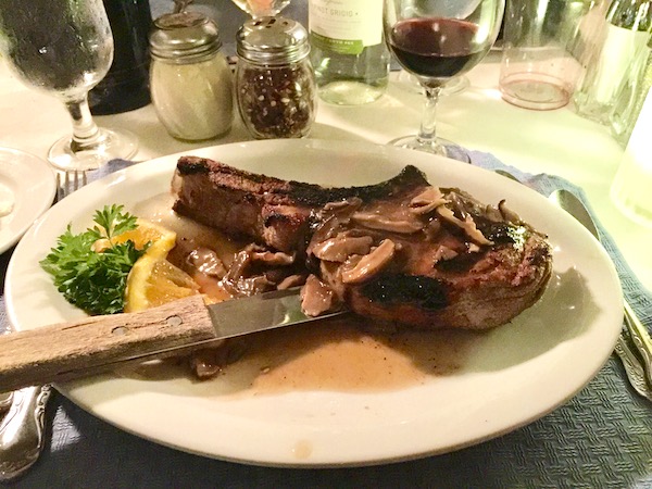 Veal Chop at Chef Vola topped with sliced mushrooms on a white plate