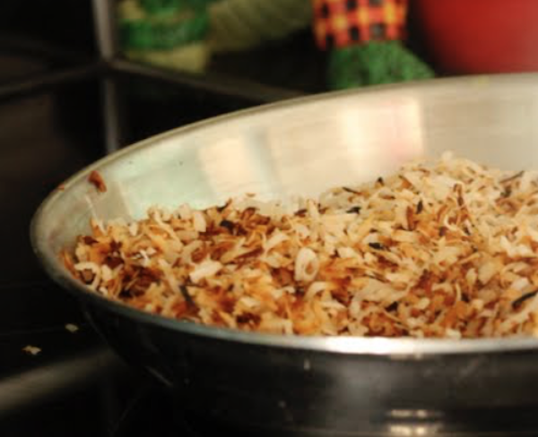 A steel bowl filled with golden brown toasted shredded coconut