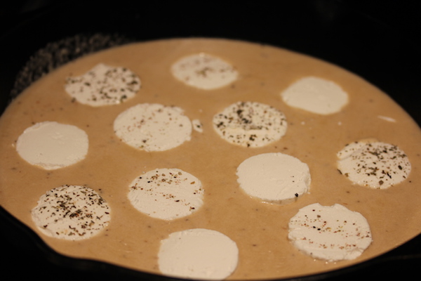A cast iron pan filled with cheese dip and large dollops of white cheese