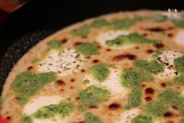 A cast iron pan filled with melted cheese dip with brown spots and green sauce