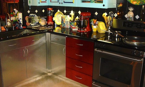 A kitchen with aqua upper cabinets and stainless steel lower cabinets, metallic red drawers and black granite countertop.