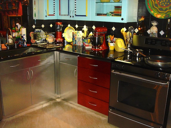 A kitchen with aqua upper cabinets and stainless steel lower cabinets, metallic red drawers and black granite countertop.