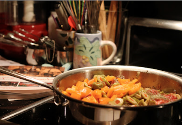 A skillet on a stove filled with chicken, olives, tomatoes
