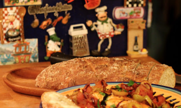 A yellow and blue dish filled with chicken cacciatore with a loaf of bread behind it.