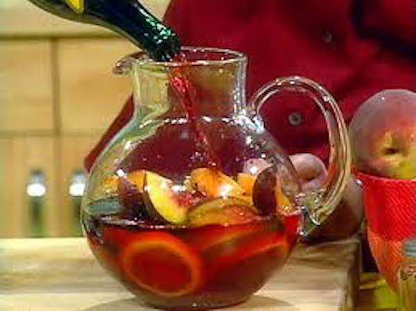 A large glass pitcher filled with fruit slice being filled with Rosé wine.