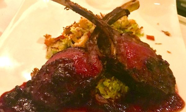 Venison chops with red sauce, sweet corn spoon bread and Brussels sprouts on a white plate