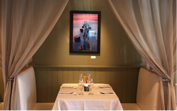 A booth with white tablecloth and tied back curtains
