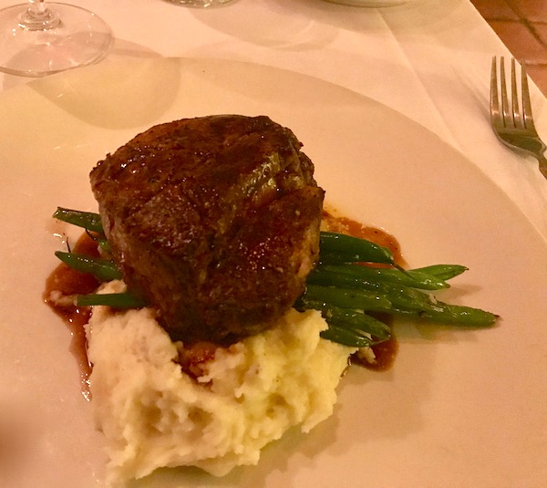 Filet mignon on a bed of mashed potatoes with green beans and jus on an ivory plate
