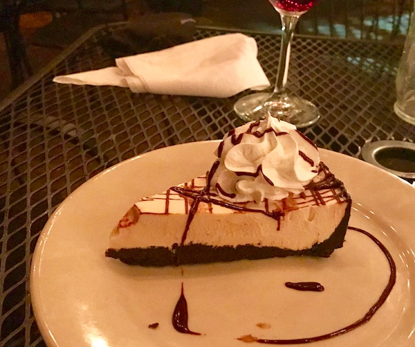 An ivory plate with a wedge of peanut butter pie topped with a rosette of whipped cream and drizzled with chocolate