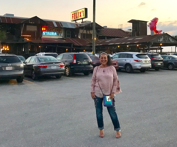 A woman in a pink top and jeans standing in a parking lot in front of a restaurant