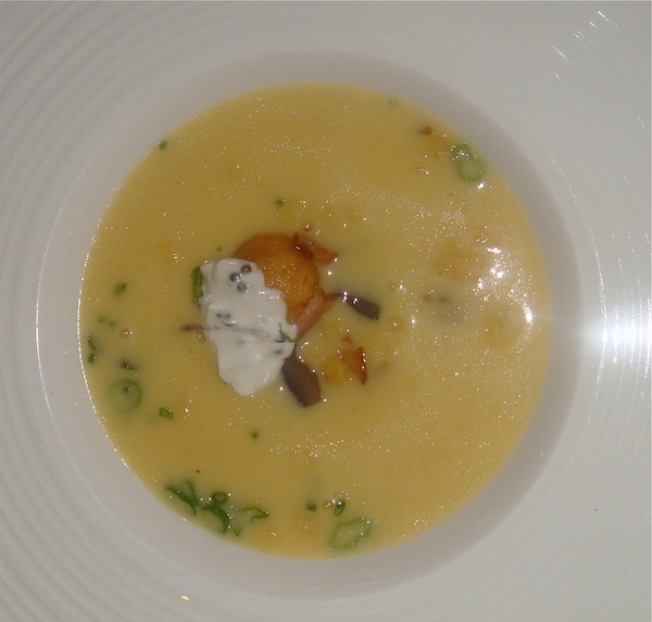 White bowl filled with golden potato soup, crouton and creme fraiche and strewn with scallion slices