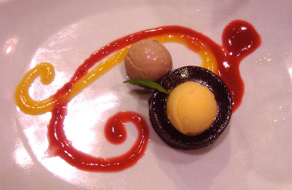 White plate with red and yellow swirls of fruit coulis adorned with sorbets and chocolate