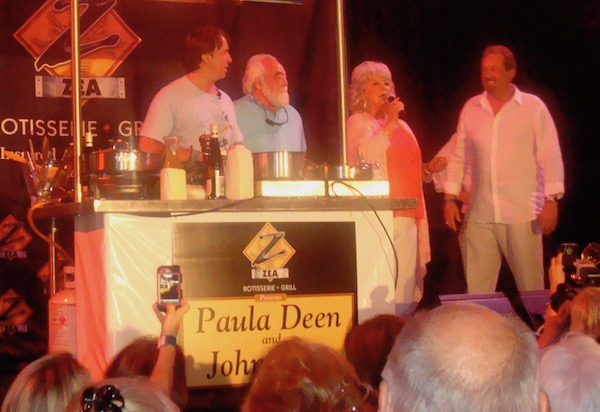 Three men and one woman at a podium with a cooking demo set up