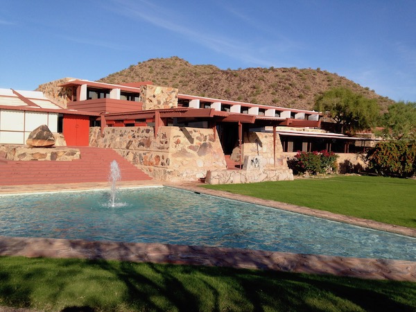 A very modern home with a reflecting pool and fountain in front.