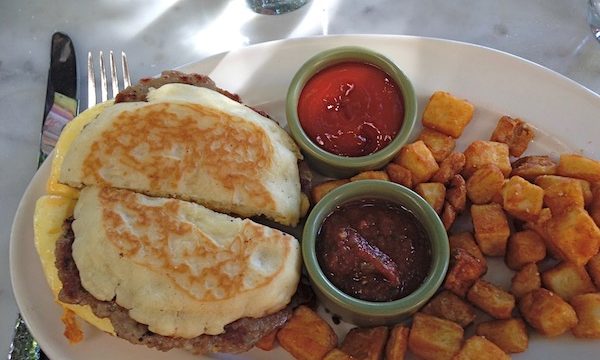 A English muffin sandwich with home fries and condiments on a white plate.
