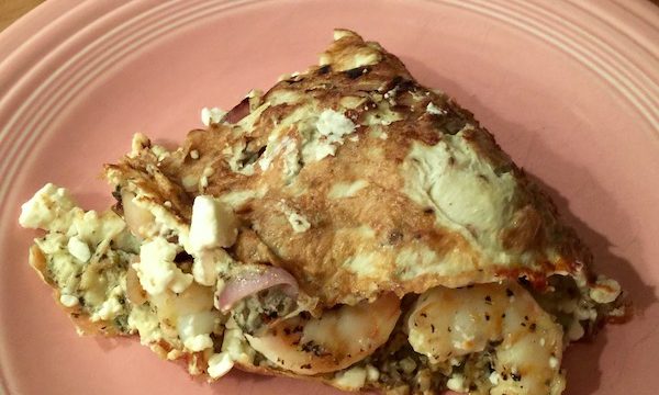 A pink dinner plate topped with a Shrimp And Feta Omelet sitting on a butcher block