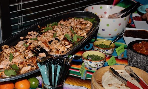 A large oval platter filled with cooked salmon and all of the accoutrements for tacos sitting on a Mexican blanket