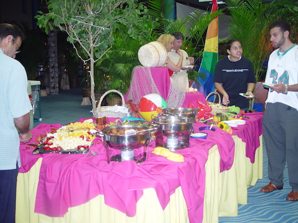A buffet table draped in hot pink and yellow with chafing dishes and serving pieces