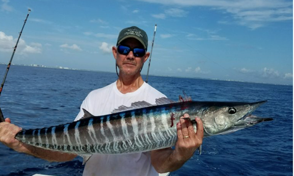 A man on a boat holding a large Wahoo fish.