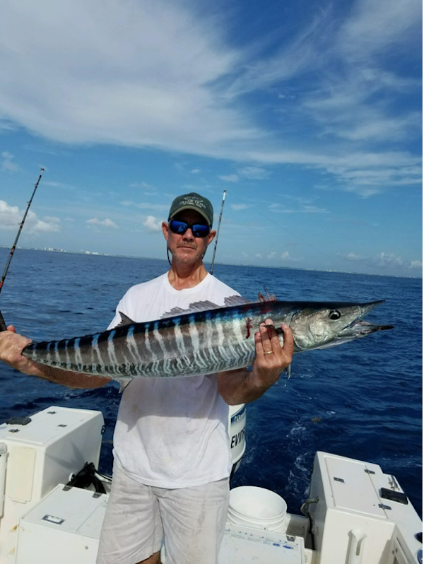 A man on a boat holding a large Wahoo fish.