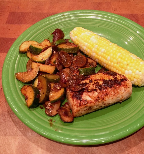 An olive colored plate topped with Wahoo Filet with Spicy Vegetables and Corn on a butcher block