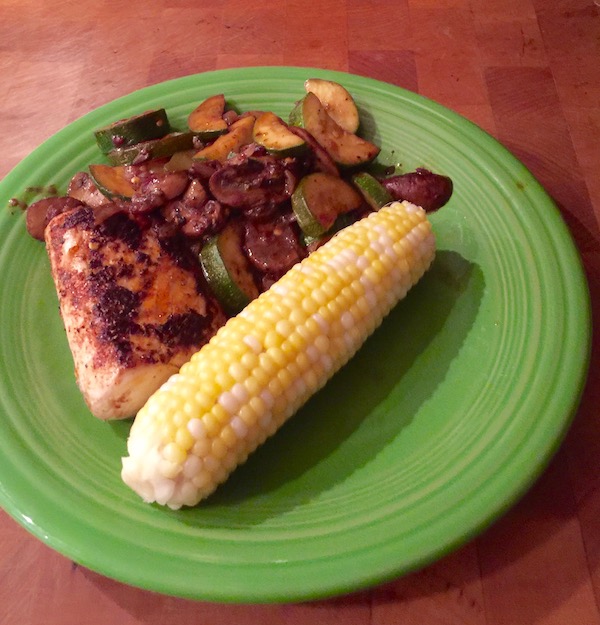 An olive colored plate topped with Wahoo Filet with Spicy Vegetables and Corn on a butcher block
