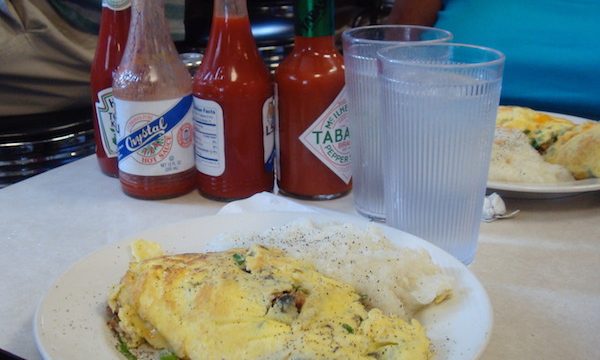 white plate with huge omelet and an assortment of hot sauce bottles