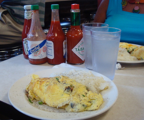 white plate with huge omelet and an assortment of hot sauce bottles