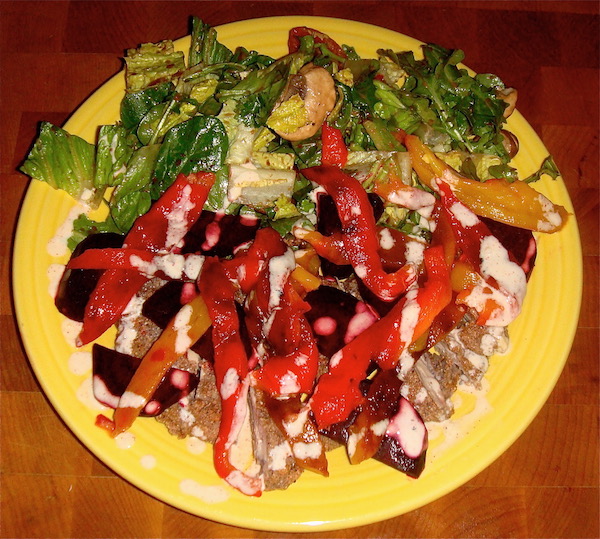 Yellow dinner plate on maple wood the plate piled high with red peppers, blue corn fried chicken and salad greens