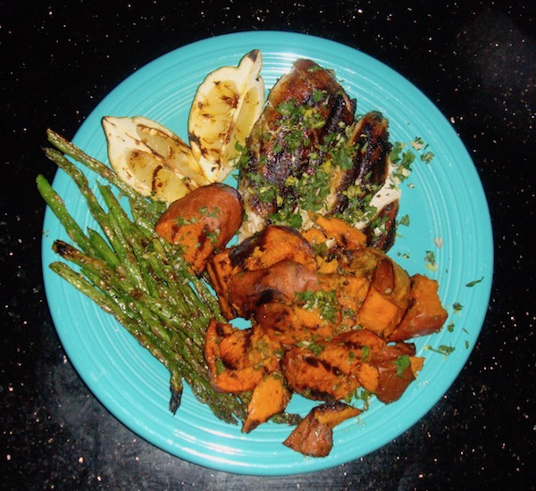 Turquoise dinner plate on black placemat filled with grilled chicken, asparagus, chunks of sweet potato and two lemon wedges