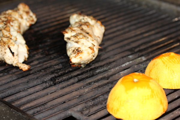 Chicken breasts and orange halves on a grill grate cooking.