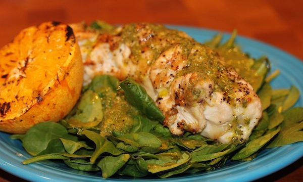 Blue dinner plate filled with fresh spinach salad in front, a grilled stuffed chicken breast behind and a grilled orange half on left side of plate