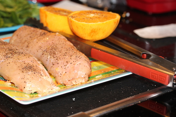 Sheet pan holding raw stuffed chicken breasts, 2 orange halve and a pair of red handled tongs