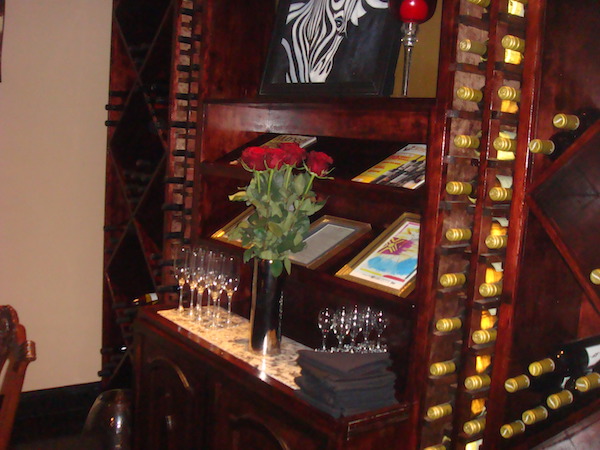 A dark wood wine storage and serving cabinet with wine glassed and a vase of red roses