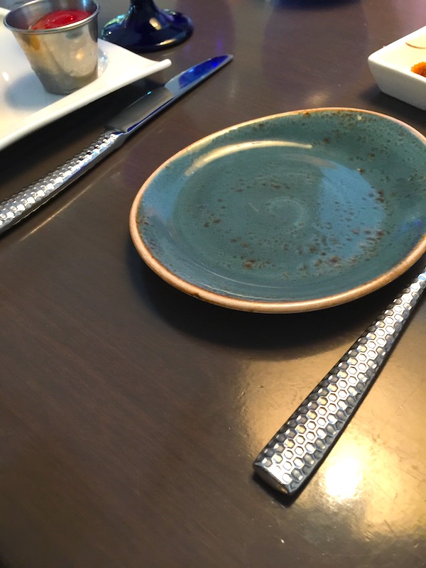 Hand made ceramic plate in teal with tan edge and hammered stainless flatware on a table
