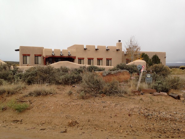 At the back of a large expanse of dirt is a very large Mexican style home.