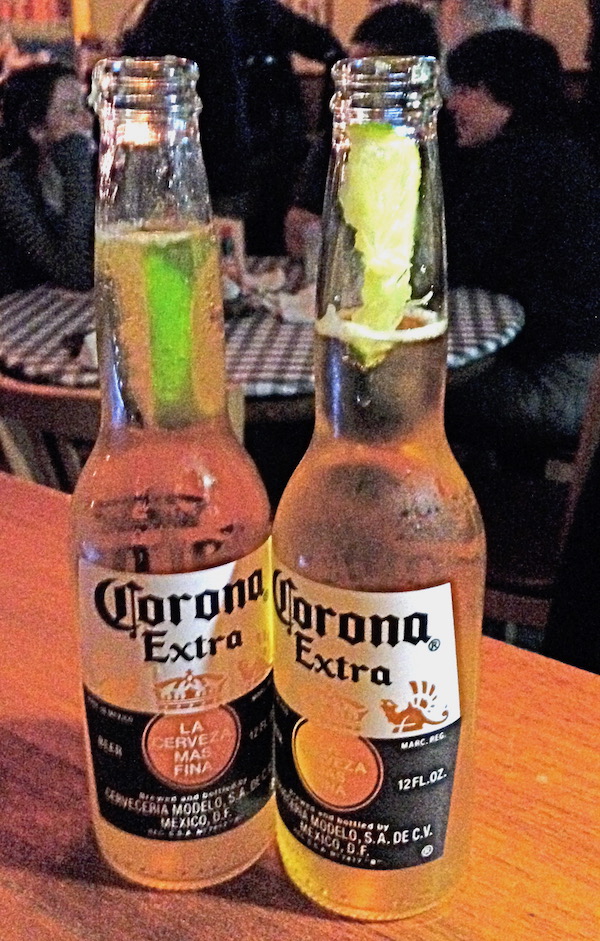 A wood table with two bottles of Corona Extra and lime wedges in the opening.