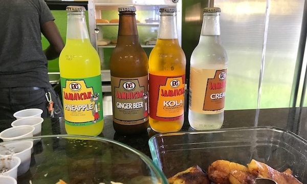 Soda bottles lined up on a counter with food in front.
