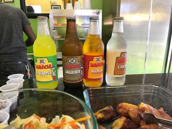 Soda bottles lined up on a counter with food in front.