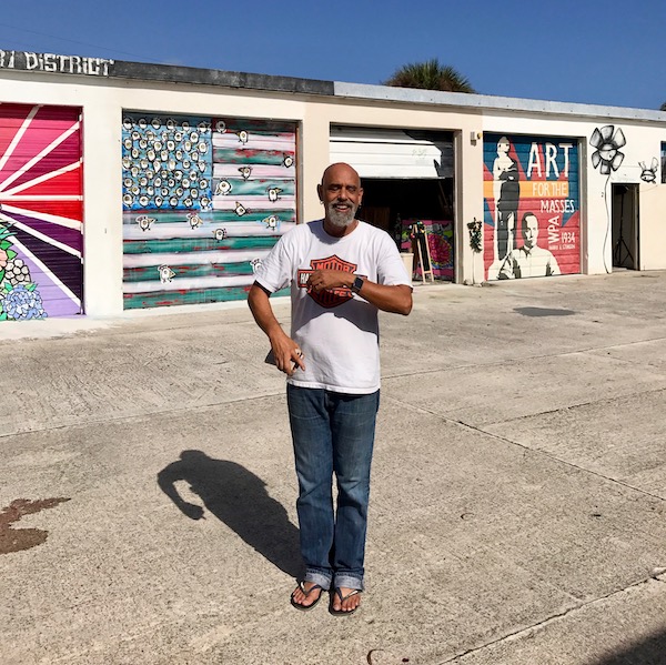 A man in front of warehouse garages with murals on the doors